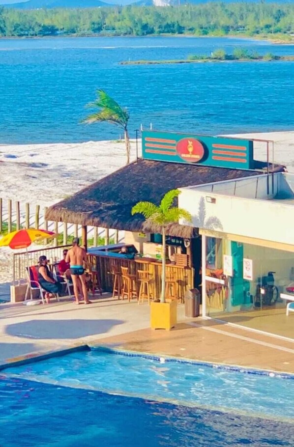 A beachfront bar with a pool, outdoor seating, and a view of the sea.