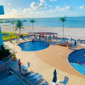 A pool area with two swimming pools, lounge chairs, and a beach view.