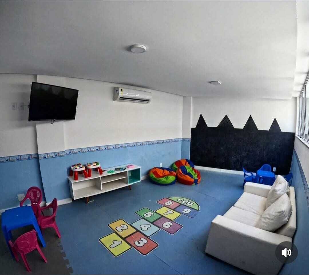 Un espace de jeux pour enfants avec un canapé, des tapis de jeu colorés et un téléviseur fixé au mur.