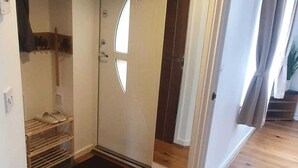 Una habitación con piso de madera, una puerta blanca de diseño único, un zapatero pequeño y un felpudo negro.