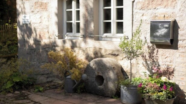 A stone building with two arched windows, a stone wall, and potted plants. - Idyllic vacation home in the countryside in the Rhön (Oberthulba)