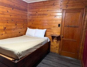 Una habitación con paneles de madera, una cama, una puerta de madera y un estante pequeño.