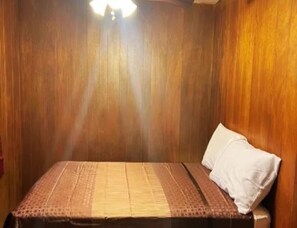 Una habitación con paredes de madera, una cama con colcha estampada y un almohadón blanco.