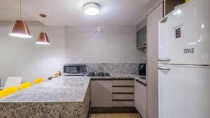 Een moderne keuken met granieten aanrecht, een ingebouwde magnetron, een fornuis en een witte koelkast.