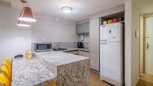 Une cuisine compacte dotée d’un plan de travail en granit, d’un four à micro-ondes, d’une machine à café et d’un réfrigérateur blanc.
