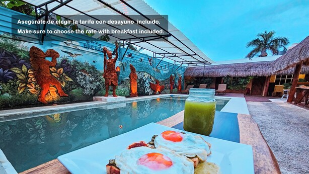 A breakfast setup with toast and eggs on a table by a pool, with a mural and a thatched-roof structure in the background. - Hotel Mayas Blue (Bacalar)