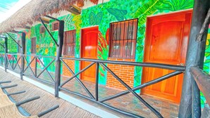 A row of rooms with wooden doors and windows, a thatched roof, and a colorful mural on the wall. - Hotel Mayas Blue (Bacalar)