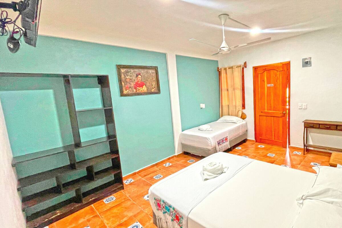 A room with a bed, a small table, a chair, a ceiling fan, a door, and a window with curtains.