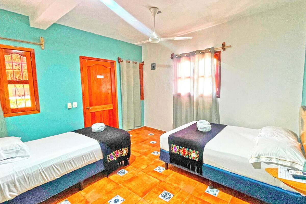 A room with two single beds, a ceiling fan, a wooden door, and a window with curtains.