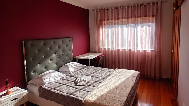 A bedroom with a large bed, a bedside table, a small desk, and a window with curtains. - A place to rest (Gualtar)