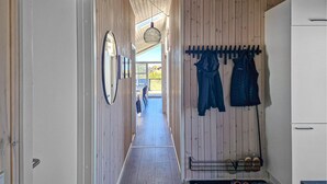 A hallway with wooden walls, a mirror, a hanging light fixture, and a rack with shoes and clothes.