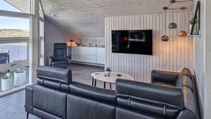 A modern outdoor living space with a black leather sofa, a dining table, and a TV mounted on the wall.