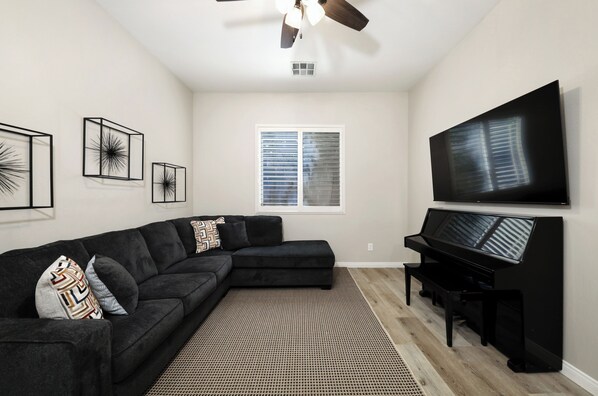 A living room with a sectional sofa, a piano, a flat-screen TV, and abstract wall art.