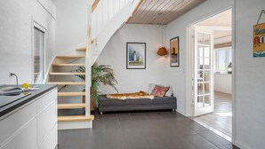 Un intérieur moderne avec un escalier, un canapé agrémenté d’un plaid en fausse fourrure et un coin repas visible à travers une porte ouverte.