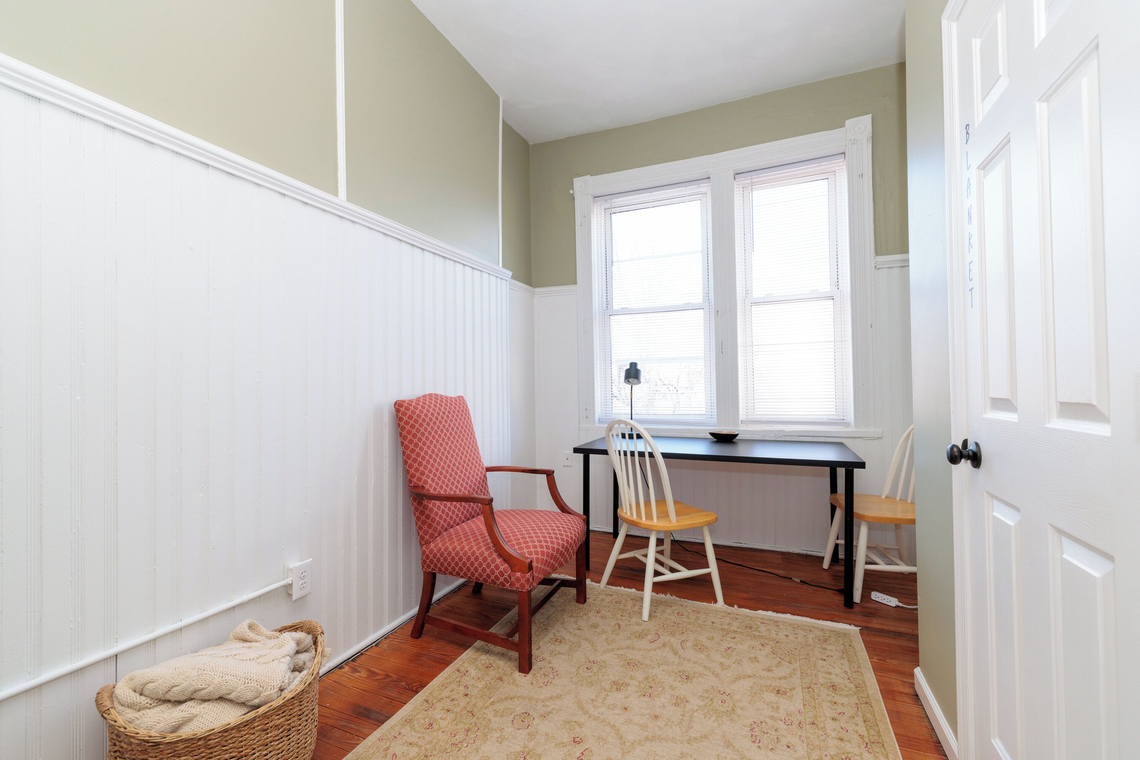Een kamer met een houten vloer, een witte radiator, een bureau met stoel en een rieten mand.