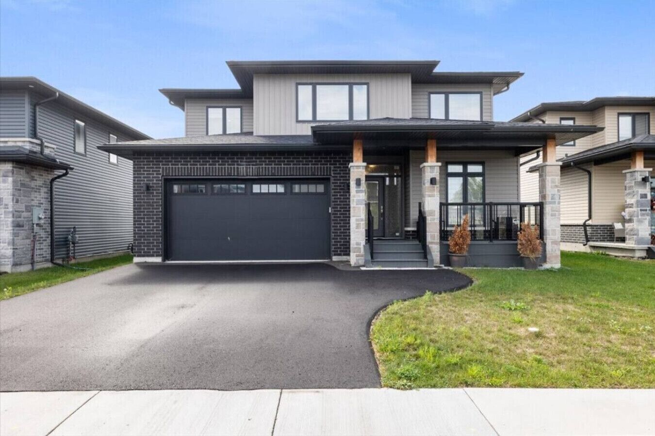 A modern two-story house with a garage, stone pillars, and a covered entryway.