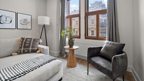 Una sala de estar moderna con un sofá gris, un sillón gris, una pequeña mesa de madera con un jarrón de flores y una lámpara de pie.