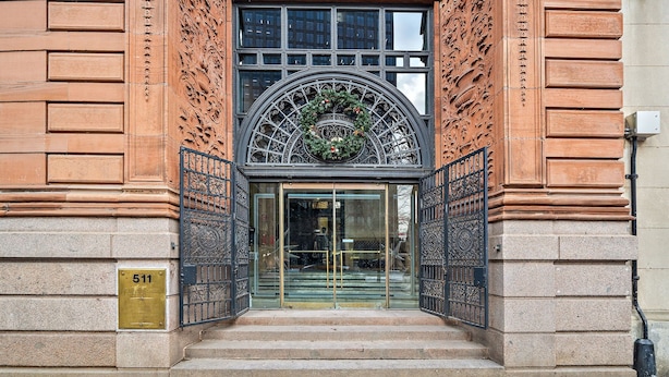 Entrada de un edificio con puerta de cristal, placa de latón con el número 511 y una reja decorativa de hierro forjado.