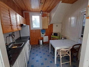 A compact kitchen with wooden cabinets, a sink, a small dining table, and a window.