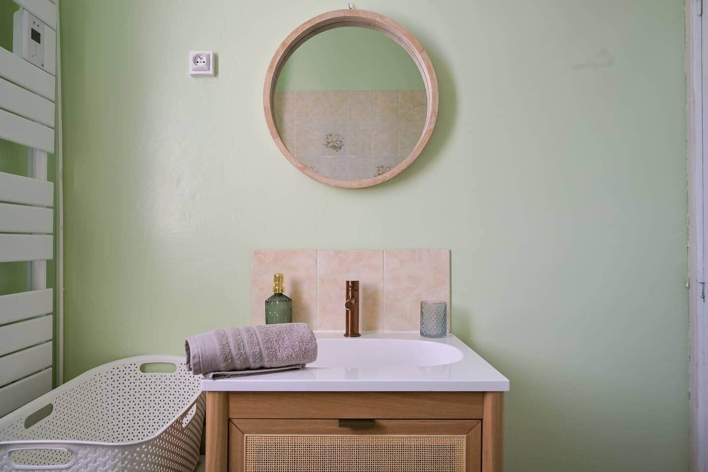 A bathroom with a round mirror, a sink, a towel, and a basket.