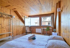 A wooden-paneled room with a bed, a chair, a desk, and a radiator.