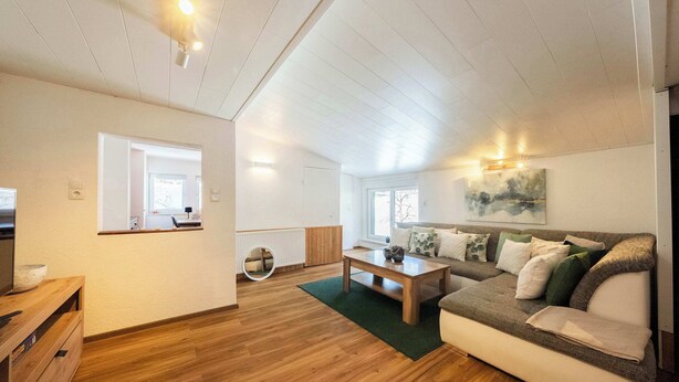 Un salon spacieux avec un plancher en bois, un canapé, une table basse et un tableau accroché au mur.