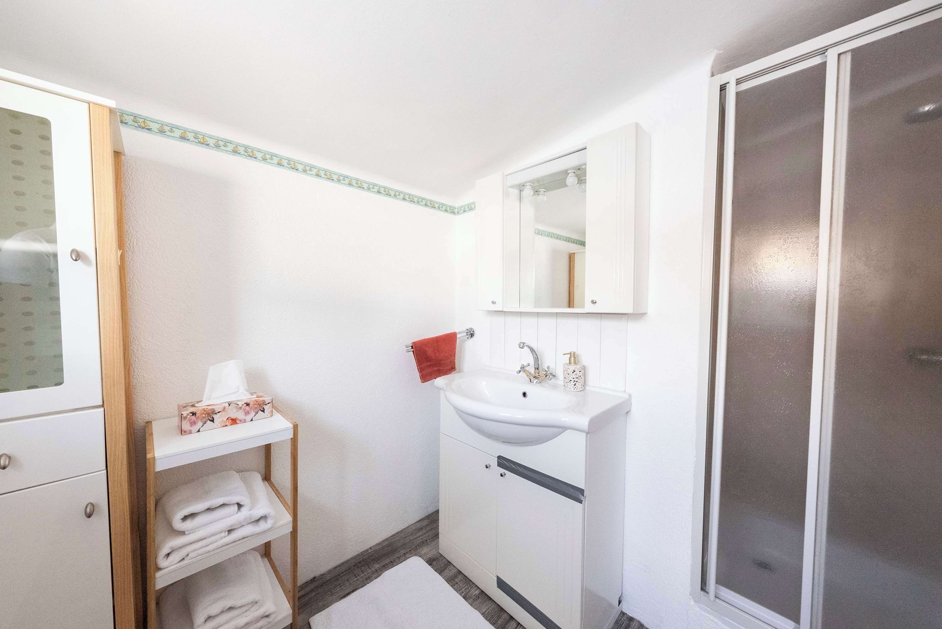 A bathroom with a white sink, a mirror, a towel rack, and a shower area.