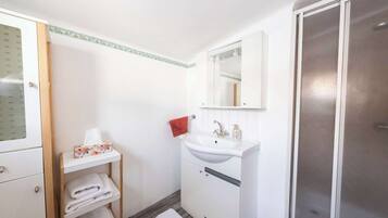 A bathroom with a white sink, a mirror, a towel rack, and a shower area.