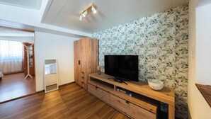 Un salon moderne avec un meuble de rangement en bois pour l’équipement audiovisuel, un téléviseur à écran plat et un papier peint à motifs floraux.