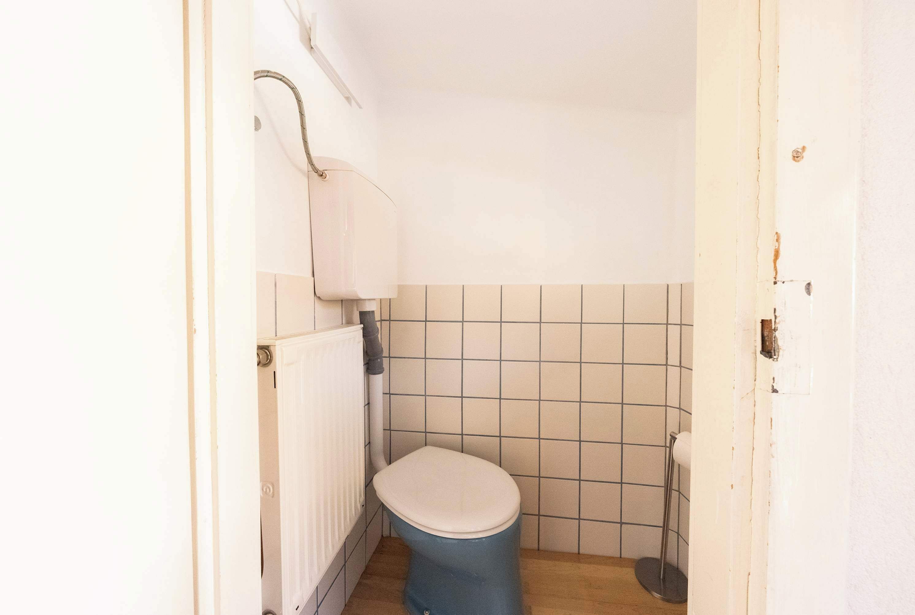 Ett litet, kompakt badrum med en toalett, ett element och kaklade väggar.