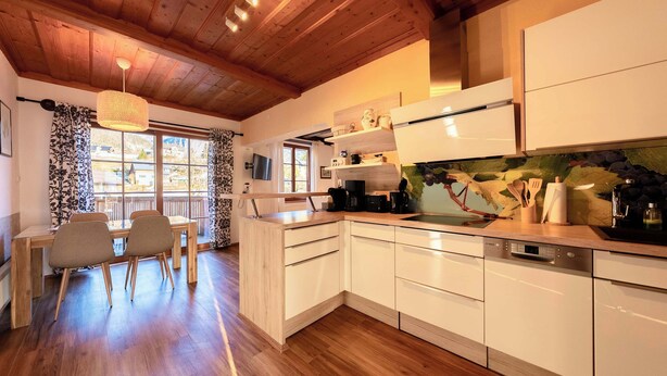 Una cocina moderna con armarios de madera, un comedor con mesa y sillas, y un amplio ventanal con cortinas.