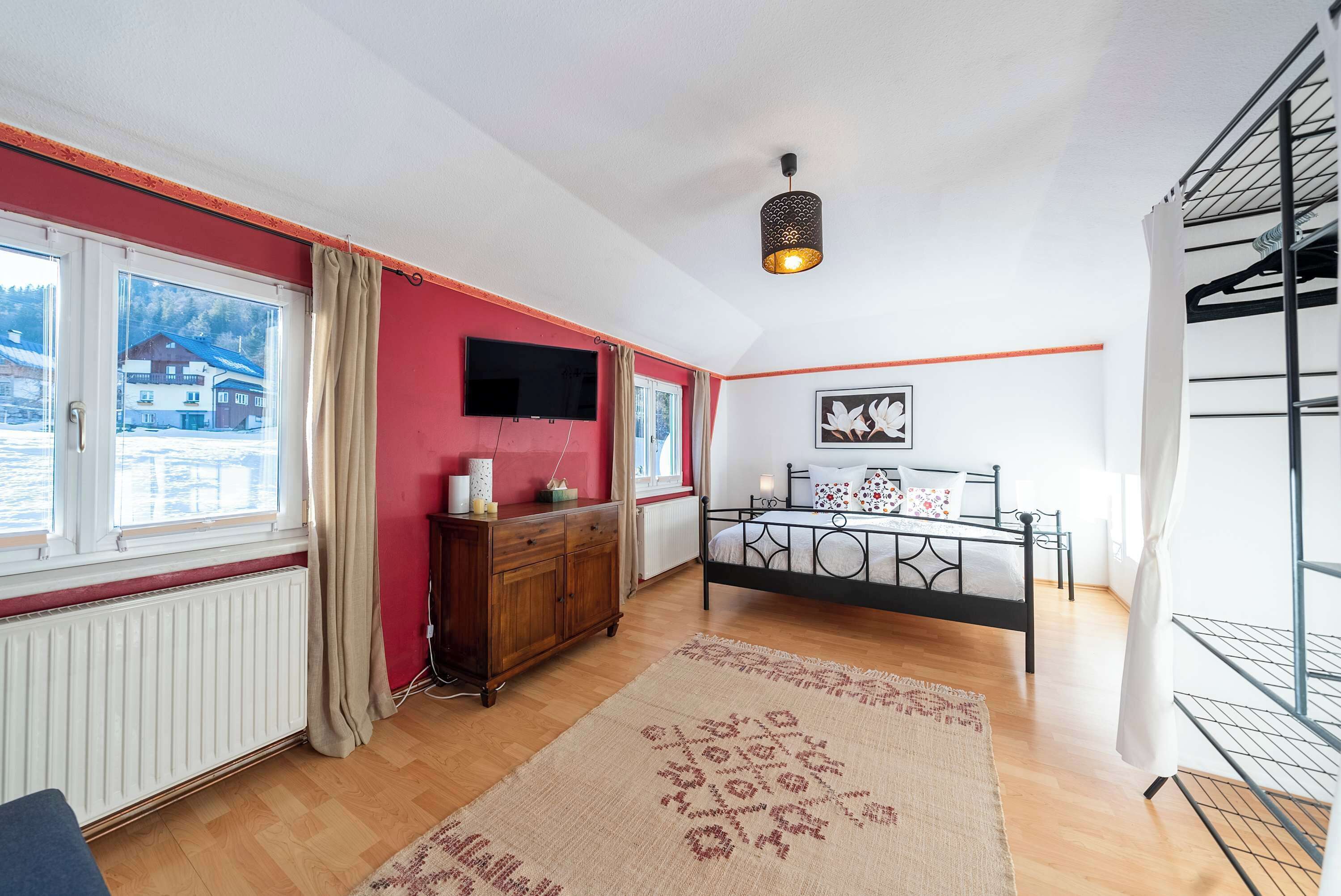 Une chambre à coucher avec un lit, une commode, une télévision et une fenêtre avec des rideaux.