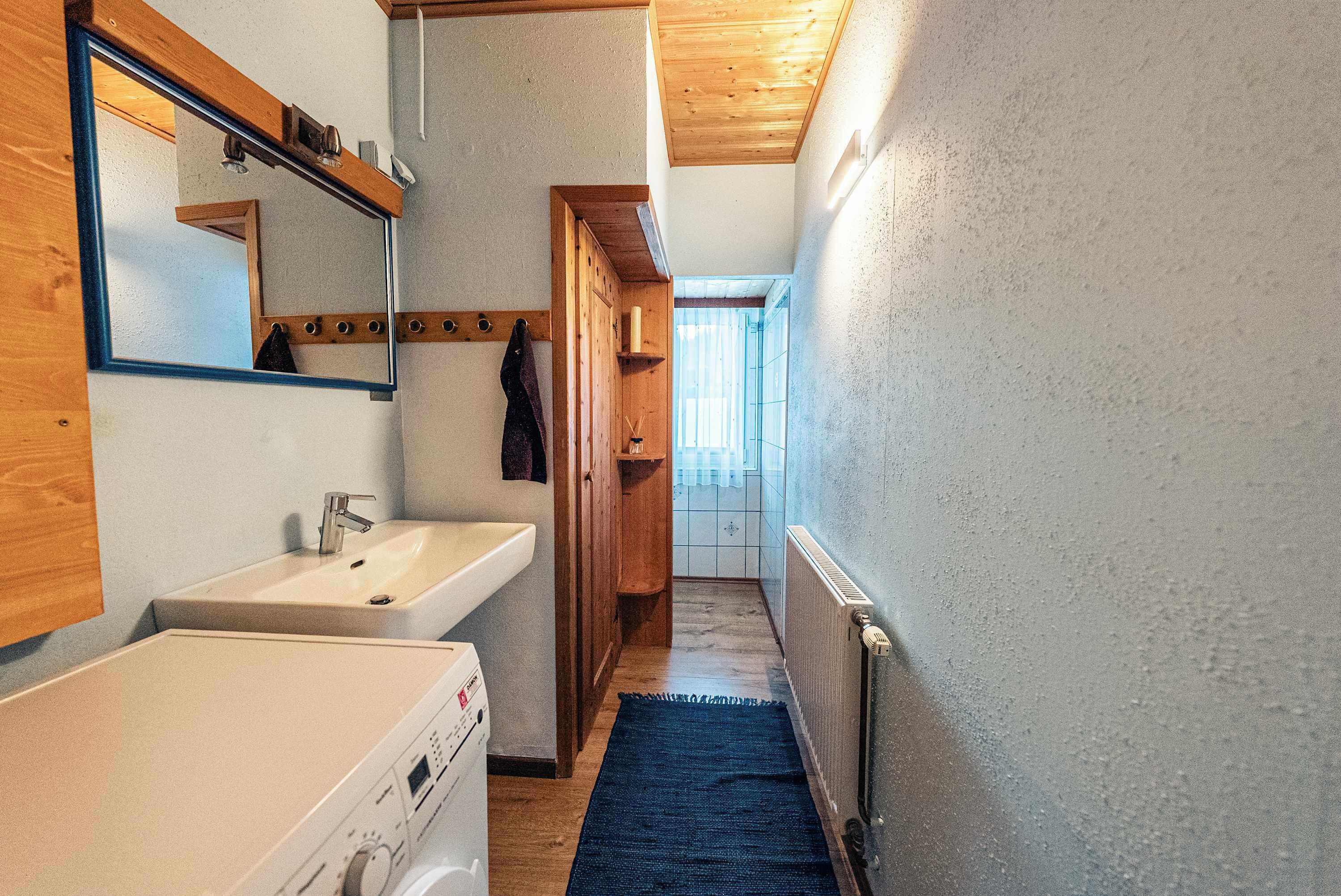 A narrow hallway with wooden flooring, a white sink, a mirror, and a radiator.