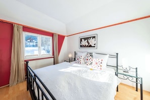Une chambre à coucher avec un lit, une fenêtre avec des rideaux, une table de chevet avec une lampe et un tableau accroché au mur.