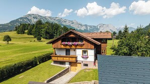 Un chalet tradicional con fachada de madera, un balcón con jardineras y vistas a montañas al fondo.
