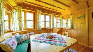 Una cabaña de madera acogedora con comedor, ventanas grandes con cortinas y vistas al exterior.
