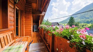 Un balcón de madera con un banco y una silla, rodeado de jardineras con flores.