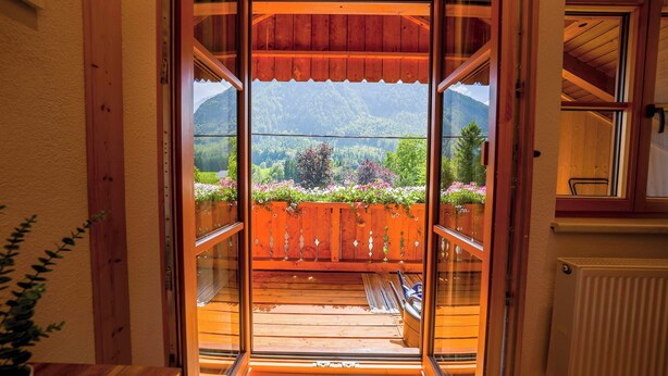 Un balcón de madera con vistas a un paisaje montañoso y una valla de madera adornada con flores.