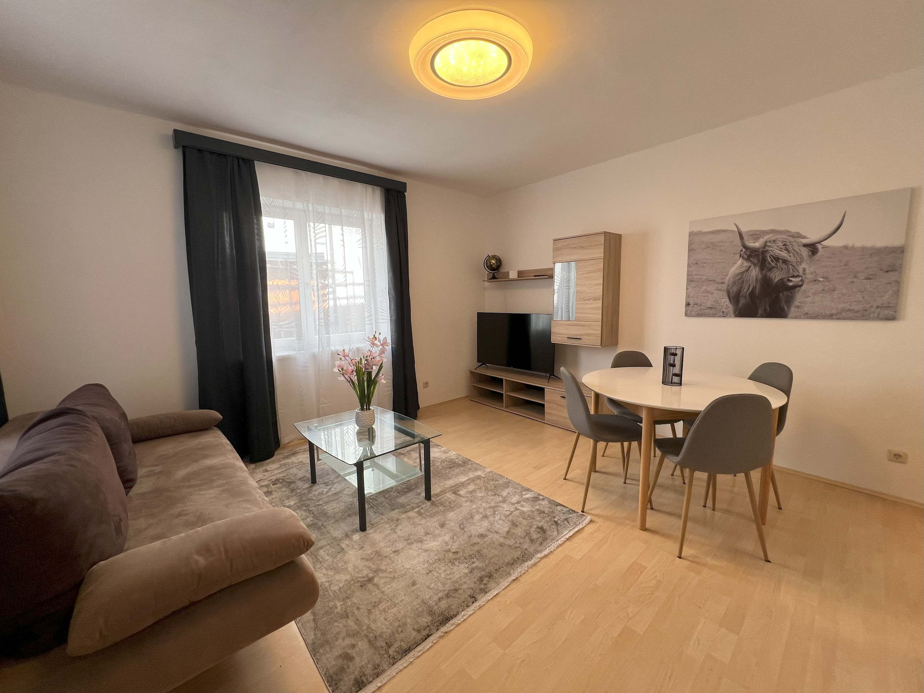 Een moderne woonkamer met een bank, een glazen salontafel, een eettafel met stoelen, een televisie en een kast.