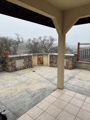 A covered patio area with stone walls, a metal door, and a view of trees in the background.