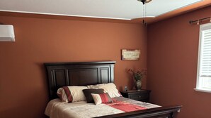 Un dormitorio con cama de madera oscura, ventilador de techo y ventana con persianas.