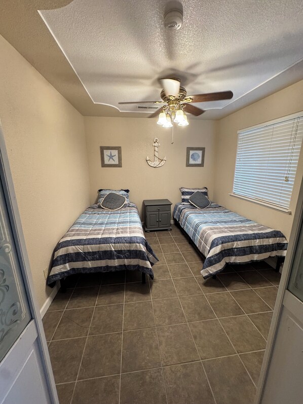 A bedroom with two beds, a ceiling fan, and a window with blinds.