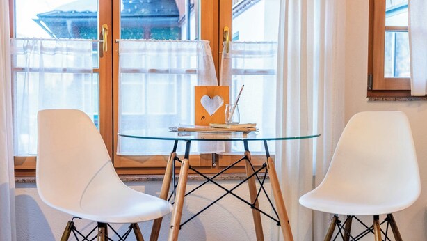 A room with two white chairs, a glass table, and a wooden heart-shaped object on the table. - Krokus Studio | Relax & Natur | Parking | Bikes (Altaussee)