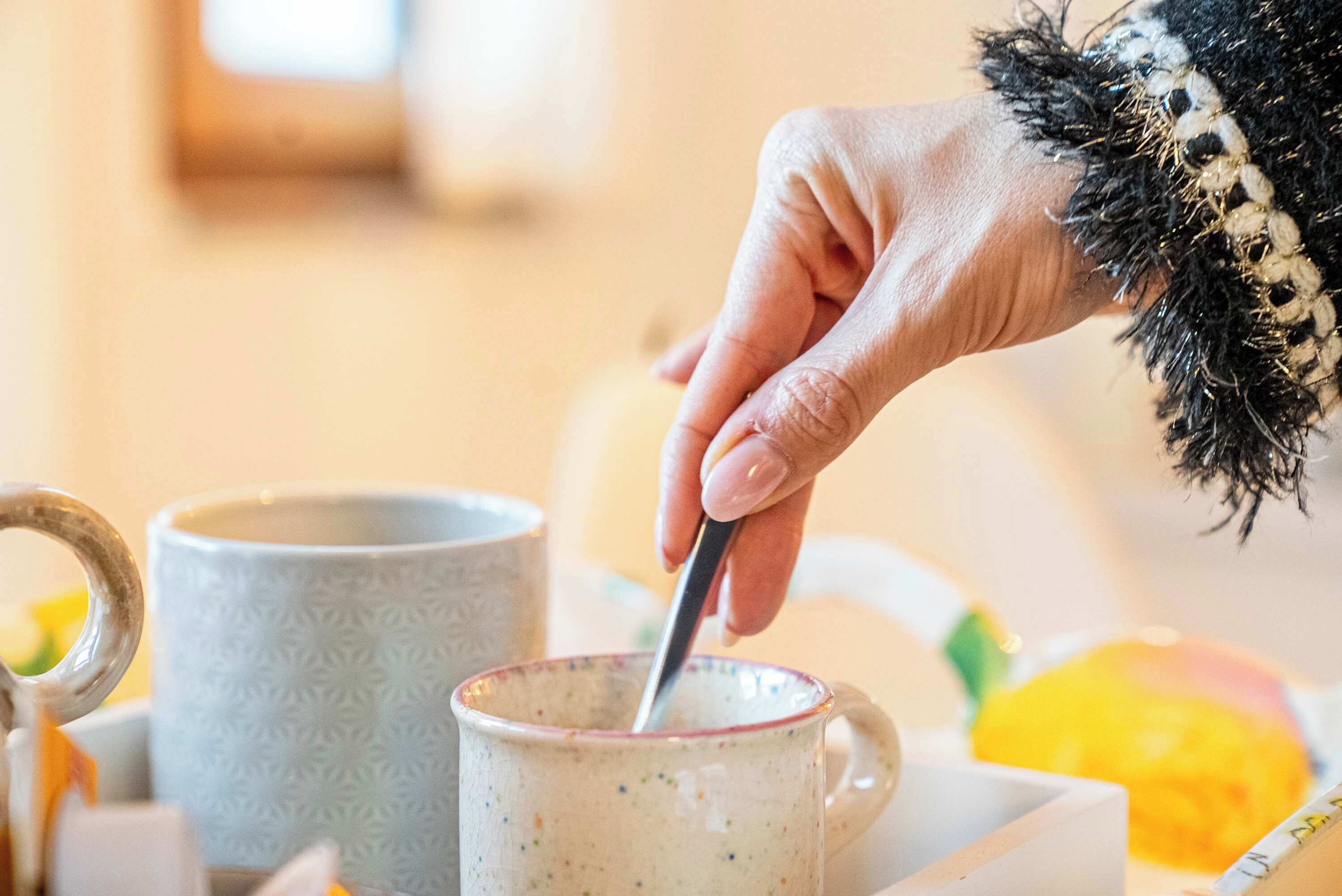 Una mano mescola una bevanda in una tazza di ceramica con manico.