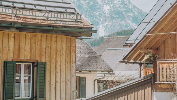 A wooden building with a sloped roof, a window with shutters, and a view of a mountain range in the background. - Strauss Suite | Kitchen | Parking | Garden (Altaussee)