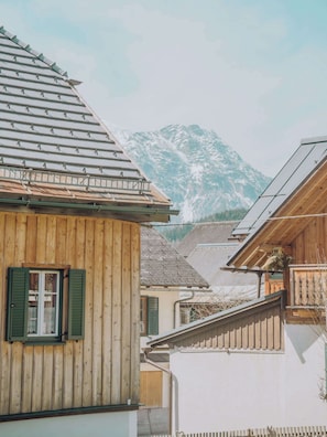 A wooden building with a sloped roof, a window with shutters, and a view of a mountain range in the background.