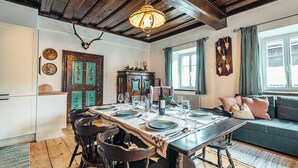 A dining area with a wooden table set for four, chairs, a chandelier, and a sofa with cushions. - Strauss Suite | Kitchen | Parking | Garden (Altaussee)