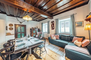 A cozy room with a wooden ceiling, a dining table set for four, a sofa, and a window with curtains.