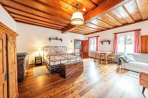 A wooden-floored room with a bed, a sofa, a dining table, and a chandelier.