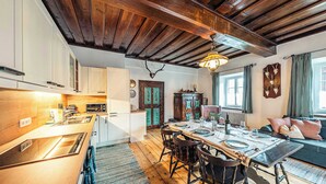 A dining area with a wooden table set for four, a kitchen with white cabinets, and a rustic ceiling. - Strauss Suite | Kitchen | Parking | Garden (Altaussee)